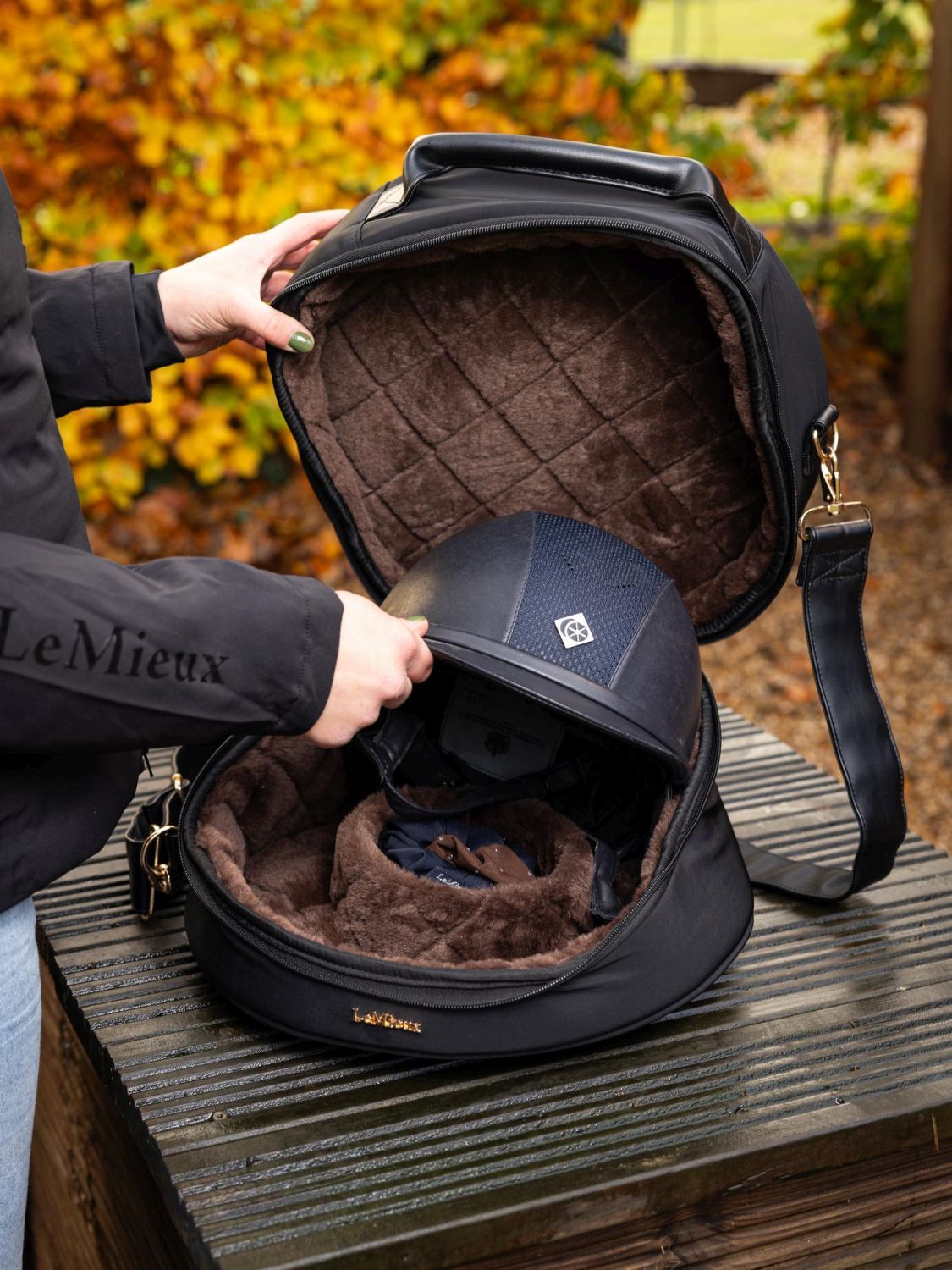 Reiterin legt ihren Reithelm in die LeMieux Helmtasche Luxe Schwarz mit goldenen Details – edle, gepolsterte Reithelm Tasche für sicheren Transport.