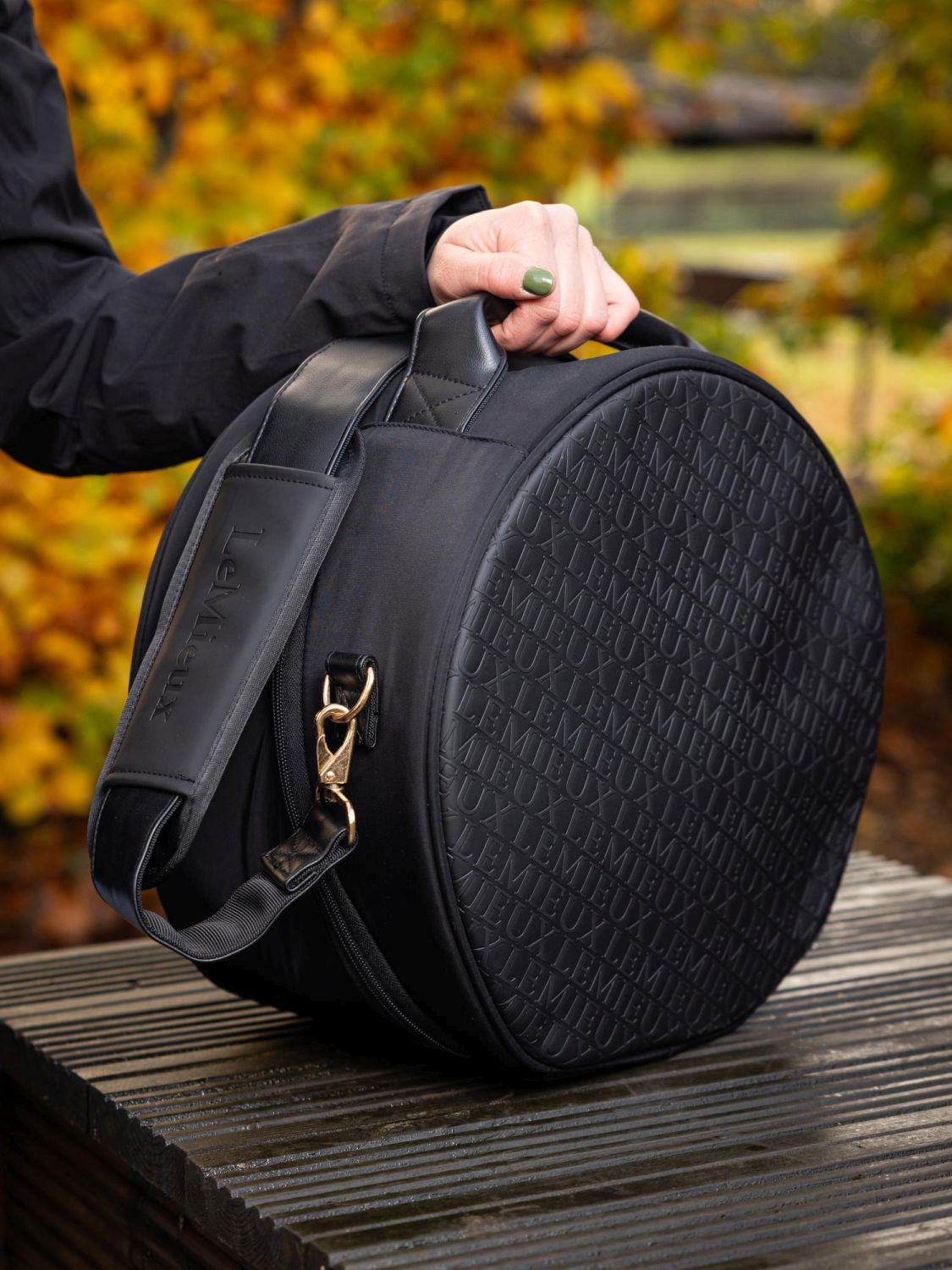 Reiterin trägt die schwarze LeMieux Helmtasche Luxe im Stall – stilvoller Schutz und Transport für den Reithelm. Reiterin nutzt den gerollten Handgriff. Tasche ist aufgerichtet.