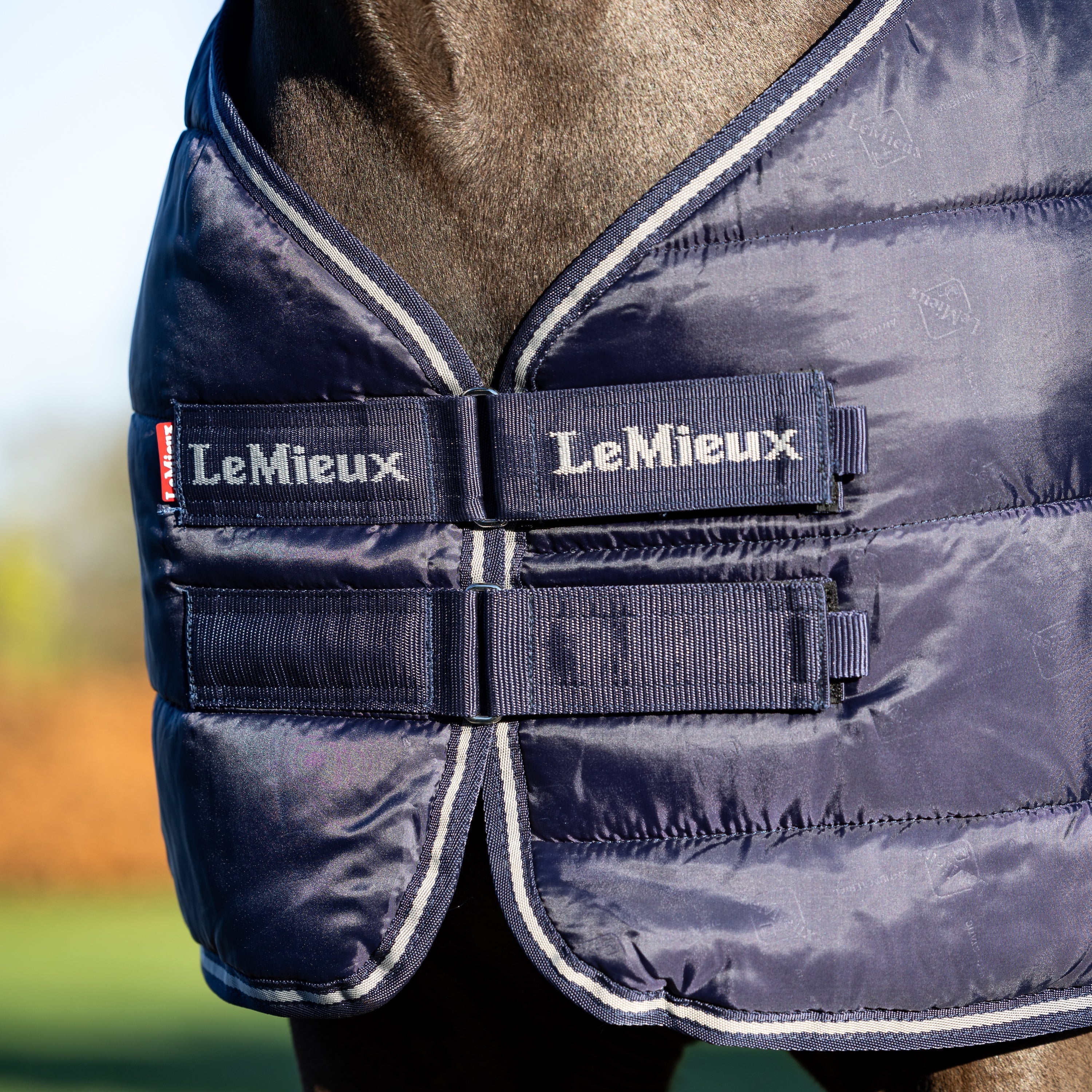 Detailbild des Brustverschlusses mit Klettverschluss an der LeMieux Unterdecke 100 g Navy pferdefreundlicher Komfort störungsfrei beim Liegen und Wälzen hält die Decke sicher in Position ideal als Liner-System mit nahtlos befestigter zweiter Linerdecke sorgt für optimale Stabilität und Flexibilität beim Layering von Pferdedecken. Das Lemieux Logo ist am Klettverschluss zu sehen.