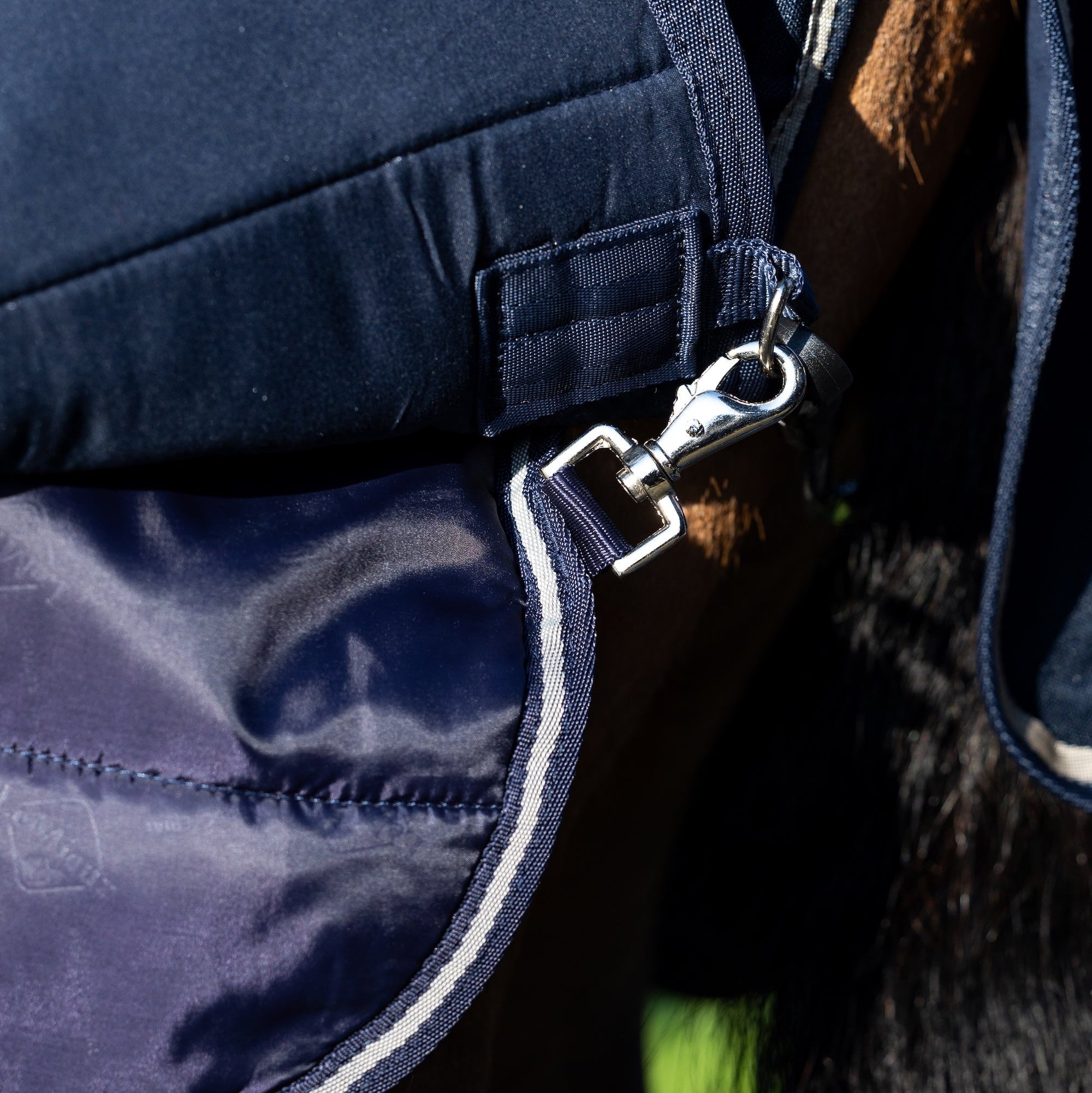 Detailaufnahme am Pferd der Schnellverschluss-Karabiner im Bereich der Hinterbeine am Deckenrock der LeMieux Unterdecke 200 g Navy. Die Karabiner sichern die Position der Unterdecke und ermöglichen die Befestigung einer zweiten Liner- oder Hauptdecke, um ein Verrutschen zu verhindern. Dieses System sorgt für flexibles, komfortables und pferdefreundliches Layering im LeMieux Pferdedecken Liner-System und bietet extra Wärme.