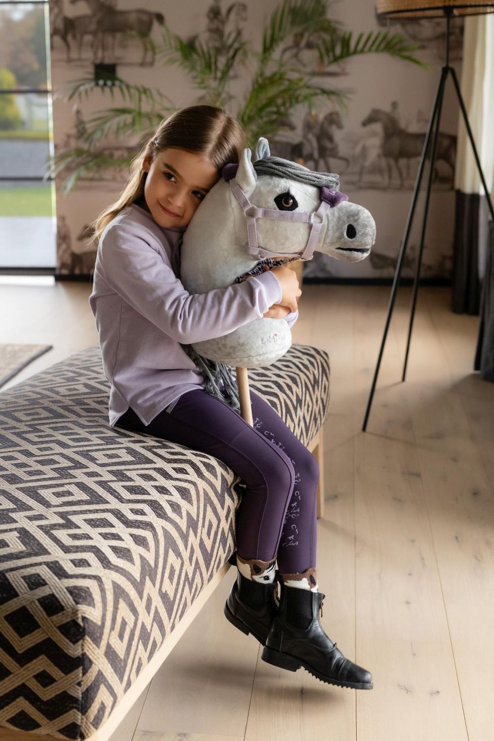 Kind mit LeMieux Hobby Horse Earl beim Kuscheln und Liebhaben im Wohnzimmer.