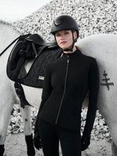 Die LeMieux Jacke Aspen Brushed Zip Through Jacket aus der stilvollen Aspen Kollektion, kombiniert mit der LeMieux Aspen Reitleggings Aspen Houndstooth mit Hahnentrittmuster wird von einer Reiterin getragen. Das Pferd ist im Partnerlook mit der Dressurschabracke Aspen Houndstooth Dressage Square ausgestattet. Passend zu den schwarzen Lemieux Loire Polo Bandagen.