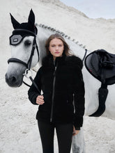 Reiterin trägt die LeMieux Aspen Puffer Jacket Black beim Führen des Pferdes – stilvolle und warme Reitjacke in Samtoptik. Die Aspen Steppjacke kann mit allen Teilen der Aspen Capsual Kollektion kombiniert werden. Hier kombiniert mit der Aspen Herringbone Fliegenmütze, Schabracke und schwarzer Lemieux Reithose.