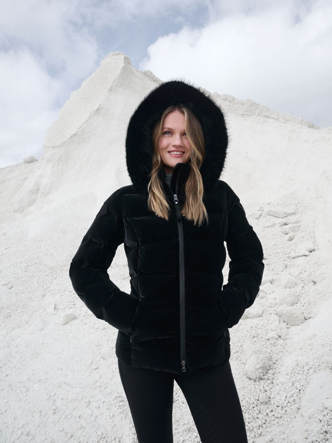Lifestyylefoto mit Model und der Aspen Jacke von Lemieux mit hochgezogener Kapuze. Das schwarze Samtdesign lässt die Steppjacke Aspen sehr weich und elegant wirken. Die Oberfläche schimmert samtig.