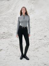 Reitmode von LeMieux – Model zeigt den schwarzen Aspen Herringbone Base Layer mit elegantem Fischgrät-Design. Halb offener Stehkragen mit Reißverschluss. Kombiniert mit schwarzer Reithose und Stiefeln. Helle und Dunkle Farben lassen sich zur Aspen Kollektion sehr gut kombinieren. Die Kapsel-Kollektion ist vielseitig nutzbar und mit anderen Kleidungsteilen von LeMieux kombinierbar.