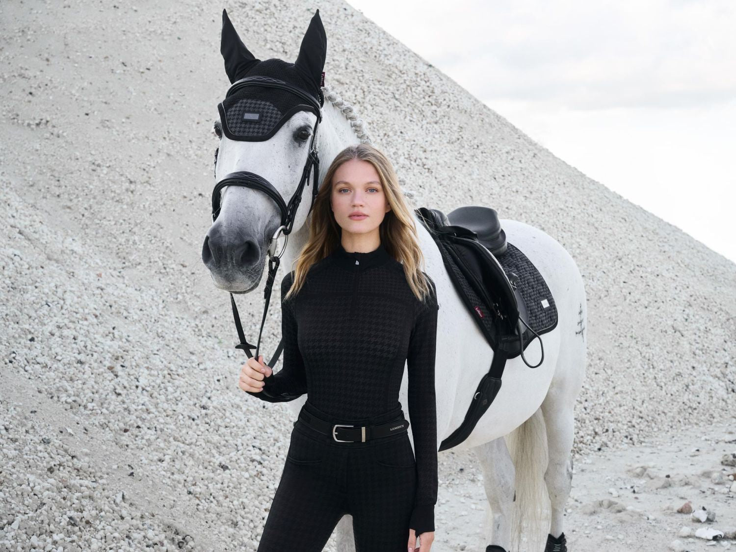 Pferd und Reiterin tragen die Aspen Kollektion mit edlem Hahnentrittmuster im Partnerlook-Schabracke Aspen, Fliegenmütze Aspen kombiniert mit dem Quarter Zip Top Aspen und einer schwarzen Reithose von Lemieux.
