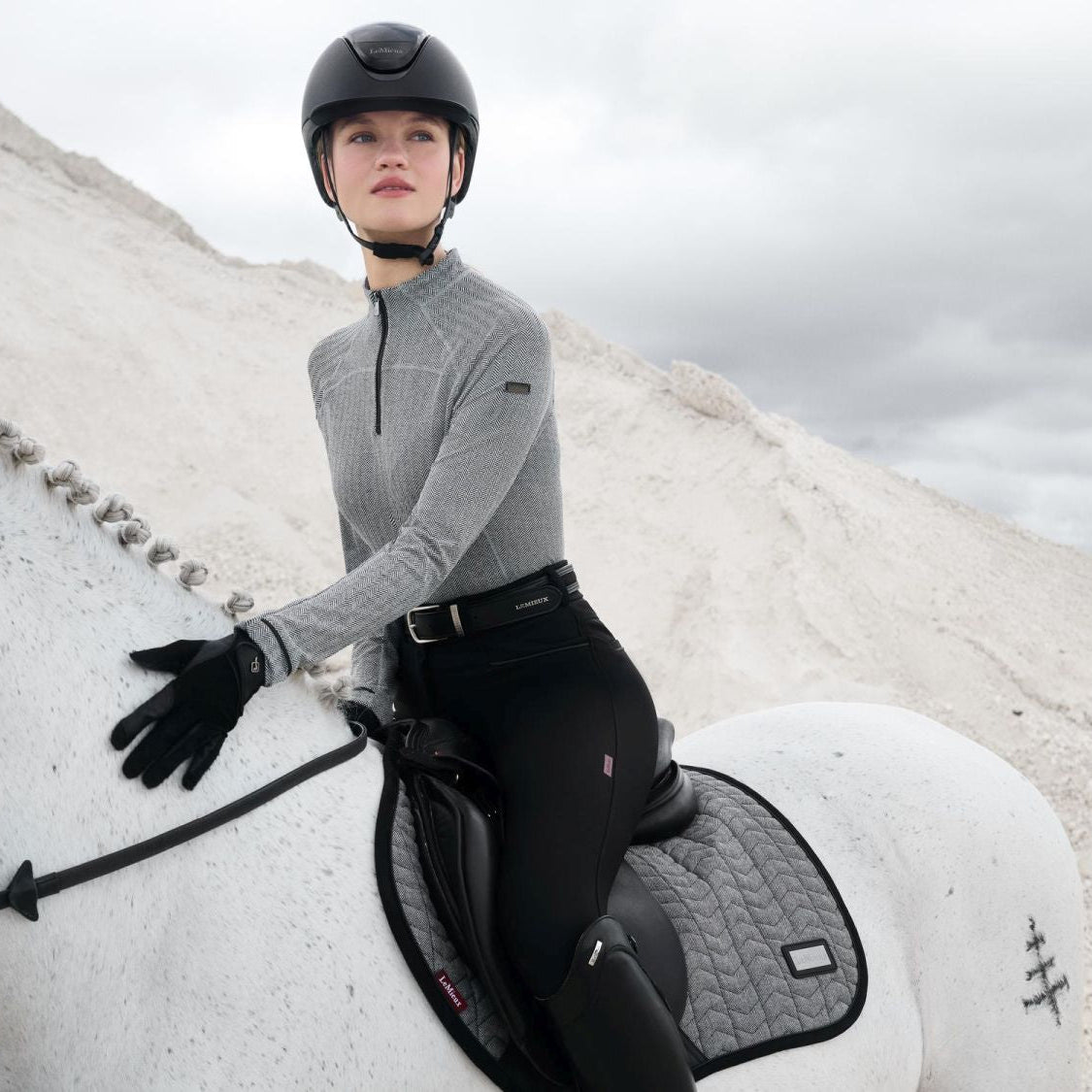 Reiterin mit Pferd in der LeMieux Aspen Kollektion – Schabracke Close Contact Square Herringbone Schwarz-Weiß. Elegante Springschabracke mit Lackpaspel und Velours-Einfassung, kombiniert mit LeMieux Reitoutfit für einen stilvollen, funktionalen Look im Springsport.
