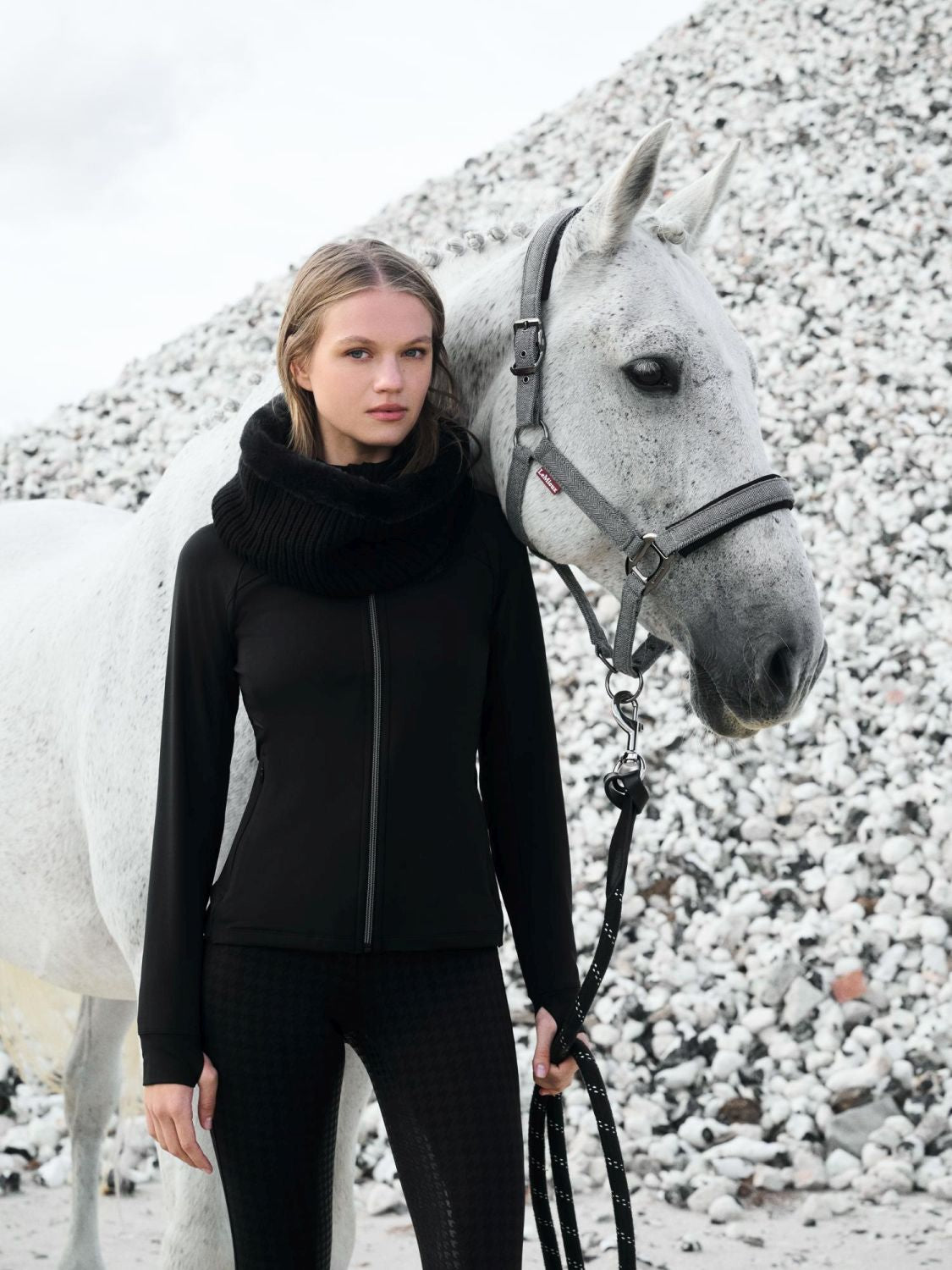 Weißes Pferd mit LeMieux Halfter Aspen Herringbone schwarz weiß, Reiterin in Lemieux Aspen Capsule Collection, elegantes Pferdehalfter mit Fischgrätmuster im Outdoor-Einsatz.