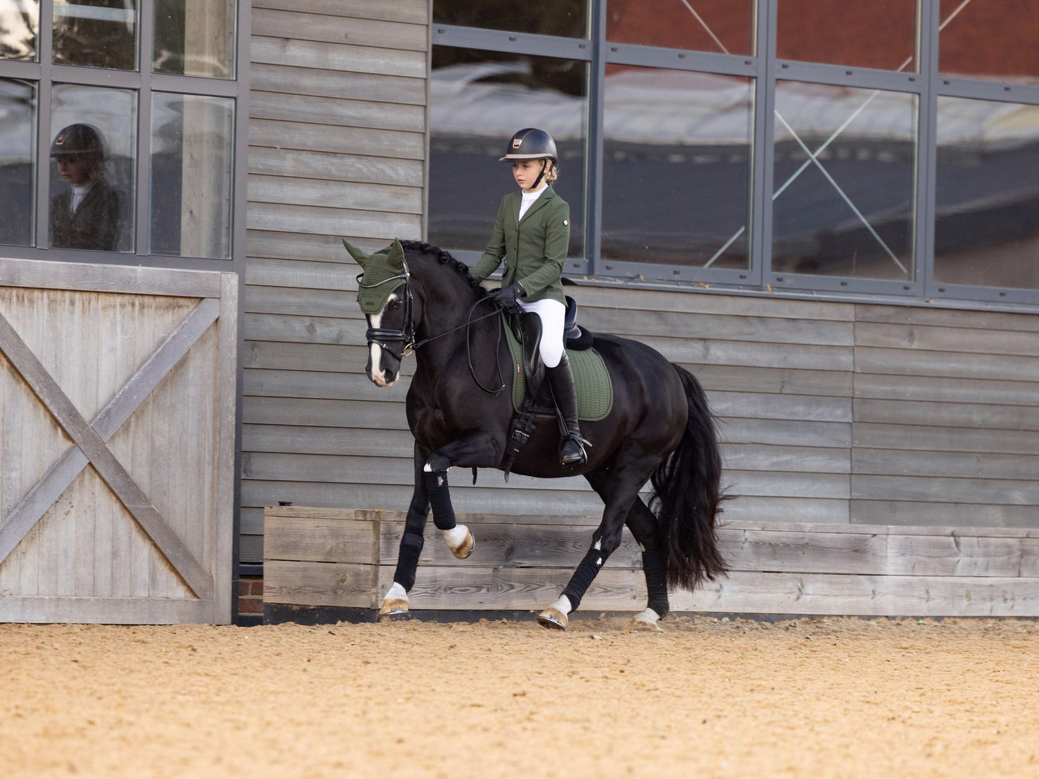 Reiterin galoppiert mit LeMieux Essence Dressage Square Pine Green, passender Fliegenmütze und Jessica Mesh Turnierjacket – Dressurschabracke in Aktion.