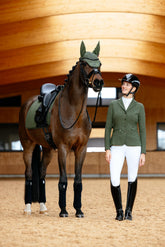 Reiterin neben Pferd mit LeMieux Essence Dressage Square Pine Green, passender Fliegenmütze und Jessica Mesh Turnierjacket in Pine Green – Pferd trägt schwarze Loire Polo Bandagen