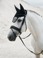 Weißes Pferd (Schimmel) mit Trense trägt die LeMieux Fliegenmütze Aspen Herringbone Black – edle Reitfliegenhaube im Fischgrätmuster mit perfekter Passform und stilvollen Lackdetails. Luxuriöser Insektenschutz und elegante Ergänzung zur Aspen Kollektion.