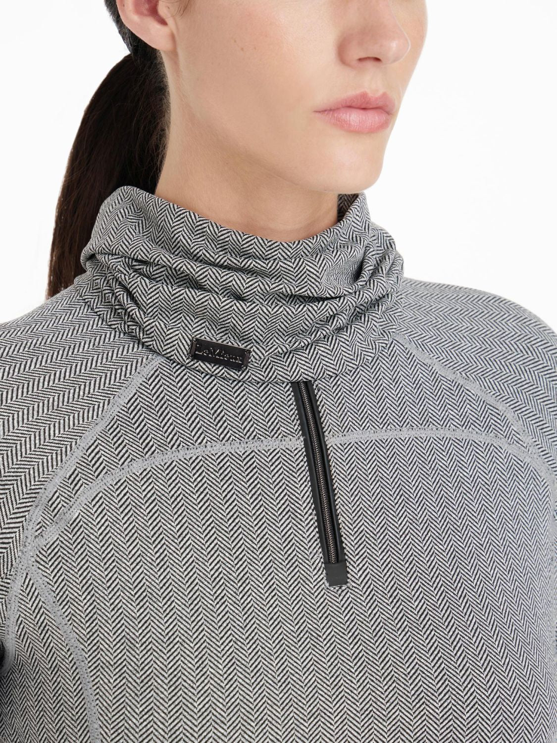 Der LeMieux Snood Aspen Herringbone mit Fischgrätmuster wird von dem Model kombiniert mit dem Aspen Herringbone Base Layer von Lemieux getragen. Der leichte Schlauchschal liegt locker um den Hals.Das Fischgrätmuster erinnert an die Gräten eines Fisches.