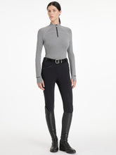 Reiterin kombiniert den LeMieux Aspen Herringbone Base Layer Black mit einer schwarzen LeMieux Reithose, Gürtel und Reitstiefel. Dadurch wirkt das edle Fischgrätmuster wie ein zeitloses Design. An den Ärmeln sind die Daumenlöcher zu erkennen, die das sportliche Langarmshirt sehr modern wirken lassen.