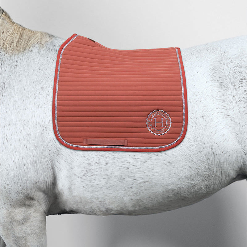 Harcour Schabracke Karembar Aurora Pink auf einem weißen Pferd (Schimmel, weißes Langhaar). Diese detailreiche Aufnahme der Dressurschabracke hebt den anatomischen Schnitt am Widerrist, die klare horizontale Steppung und die silberne Glitzer-Litze hervor. Das silberne Harcour-Logo ist deutlich sichtbar. Eine unvergleichliche Farbharmonie: Das zarte, helle Aurora Pink wirkt auf dem weißen Pferd besonders elegant und edel. Eine exklusive Pony Schabracke/Pferd Schabracke mit Glitzer für stilbewusste Reiter.