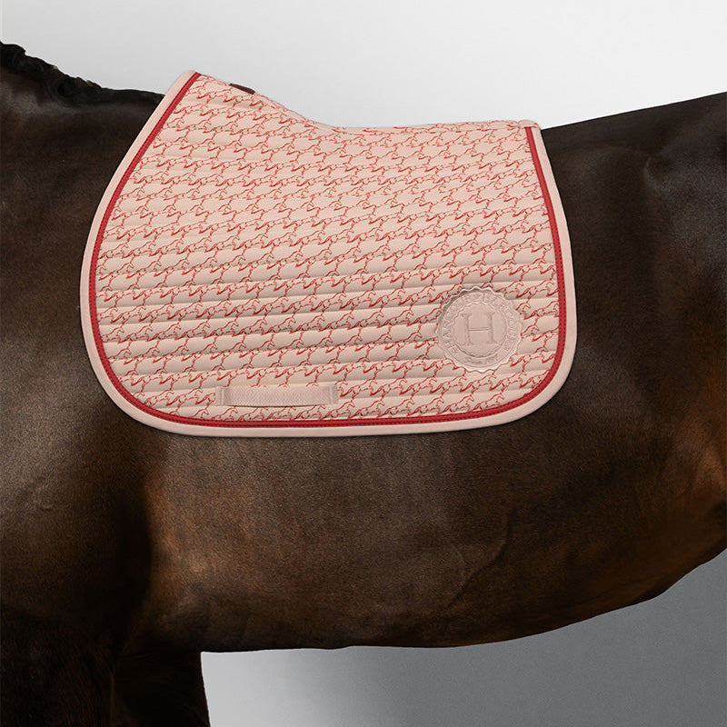 Harcour Karembar Springschabracke in Jump Shell Grapefruit auf dunkelbraunem Pferd. Die korallefarbene Litze kontrastiert edel zum dunklen Kurzhaar. Anatomisch geformt für moderne Springsättel und tägliches Training. Klare Linien durch horizontale Steppung.