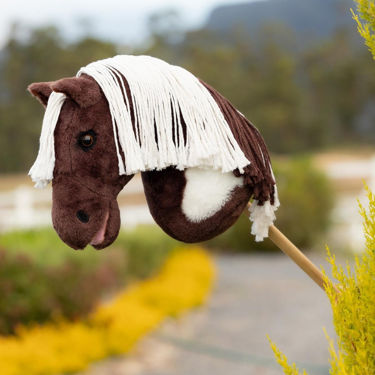Das LeMieux Hobby Horse Dazzle als detailgetreues Paint Horse im Outdoor-Einsatz auf dem Reitplatz: Ein realistisches braun-weißes Steckenpferd für Kinder und Turnierreiter zum Trainieren von Parcours, Dressur und Westernreiten.