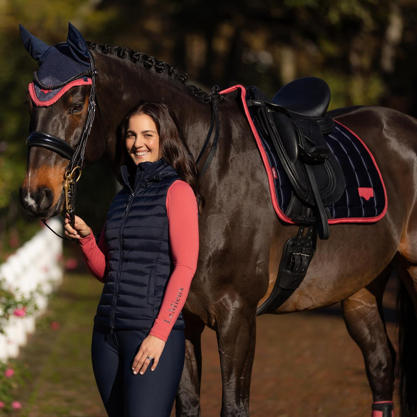 Die LeMieux Steppweste Rose Navy als ideales Hooded Puffer Gilet für Damen im Pferdesport. Diese atmungsaktive Übergangsweste bietet optimalen Windschutz und Wärme durch die umweltfreundliche Repreve®-Isolierung. Die dunkelblaue Reitweste mit horizontaler Steppung ist die perfekte Alternative zur schweren Reitjacke und garantiert maximale Armfreiheit beim Longieren oder Reiten. Ein langlebiger Bodywarmer in Navy-Blau, der durch seine wasserabweisende Funktion und den hohen Kragen besticht.