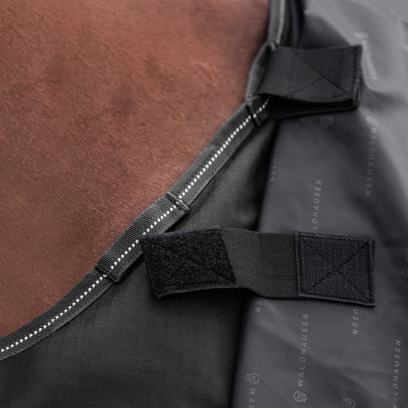 Detailansicht der Klettverschluss-Befestigung für ein separates Halsteil an der Waldhausen-Outdoordecke Arctic Light 0 g in Schwarz aus 600D Ripstop. Die integrierten Klettverbindungen ermöglichen das einfache Anbringen eines passenden Arctic-Halsteils zum Schutz von Hals und Mähne vor Regen, Wind und Nässe. Das modulare System bietet flexibles Pferdedeckenmanagement für die abgestimmten Temperaturbedingungen von Pferd und Pony im Herbst, Frühjahr und Winter.