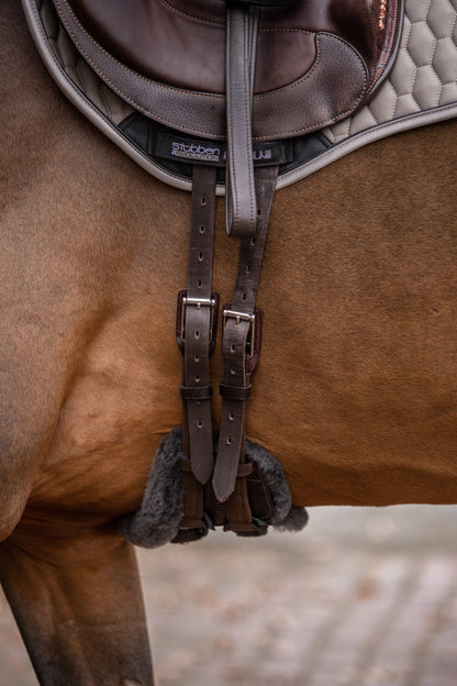 Stübben Equi-Soft Sattelgurt Ebony kombiniert mit Mattes Lammfellpolster Graphit am Pferd. korrekt gegurtet, da die braunen Gurtstrippen über dem Ellbogen des Pferdes liegen.