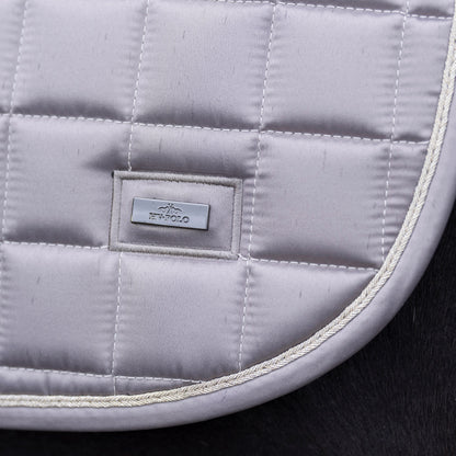 Die HV Polo Schabracke HVPDewi in der Farbe pebble ist elegant abgerundet und auf der linken Seite mit einem silbernen HV Polo Logo versehen. Das Logo ist dezent, aber sehr edel. Die goldene Kordel umrahmt die Einfassung der Dressurschabracke in der Größe Warmblut. Die Sattelunterlage HVPDewi ist ein wunderschöner Kontrast zu dunklen Pferdefellfarben.