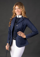 Reiterin trägt das Harry’s Horse Turnierjacket Crystal in Navy, geöffnet. Die vier Frontknöpfe sind geöffnet und zeigen den dahinterliegenden Reißverschluss, der ebenfalls geöffnet ist, für ein leichtes An- und Ausziehen. Das Jacket bleibt während des Reitens sicher geschlossen, sodass das Outfit korrekt und stilvoll für Turniere getragen werden kann. Ideal für Damen Turnierreiterinnen, Dressurreiterinnen und Reitprofis, die sich ein perfektes Turnieroutfit wünschen.