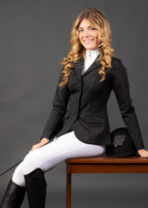 Reiterin sitzt entspannt und trägt das Harry’s Horse Turnierjacket Crystal in Schwarz, kombiniert mit weißer Turnierreithose und passendem Turniershirt. Das Jacket zeigt seine körpernahe, taillierte und feminine Schnittform und passt sich den Bewegungen der Reiterin beim Sitzen perfekt an. Ideal für Damen Turnierreiterinnen, Dressurreiterinnen und Reitabzeichenprüfung, die ein elegantes und funktionales Turnieroutfit suchen.