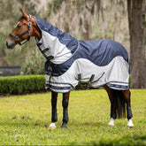 Ein Pferd auf der Weide trägt die LeMieux Fliegendecke Arika Shower-Tek in Navy mit abnehmbarem Halsteil, die als innovative Hybriddecke einen wasserdichten dunkelblauen Rückenbereich aus 600D Diamond Ripstop mit UV-Schutz gegen Regenbrand sowie seitliches graues Mikromesh für atmungsaktiven, mechanischen Schutz vor Insekten und Bremsen kombiniert.