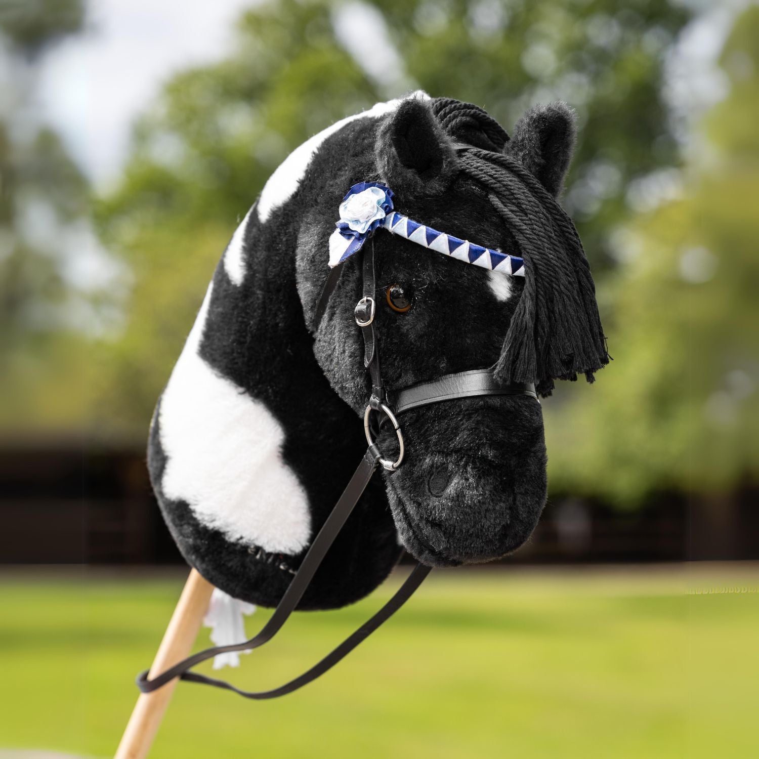 Steckenpferd Razzle mit einer Turniertrense mit blau weißer Schleife in Form einer Rosette. Perfekt gestylt für das nächste Hobby Horse Turnier. Der Rappschecke ist perfekt für alle Hobby Horse Disziplinen geeignet. Razzle zieht alle Blicke im Parcours oder Dressurviereck als Turnierpferd auf sich.
