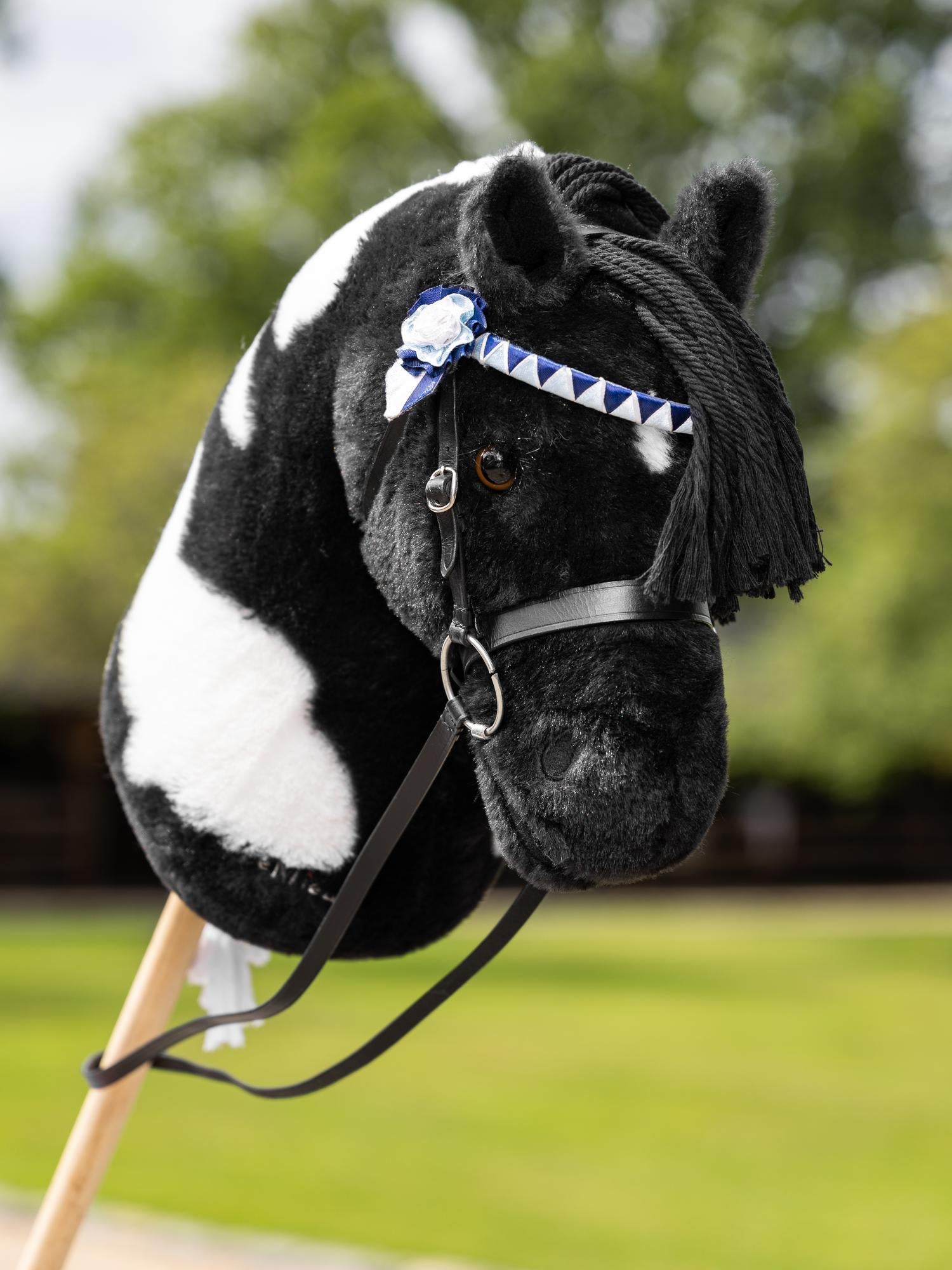 LeMieux Hobby Horse Turniertrense Show Schwarz am LeMieux Hobby Horse Razzle Realistische Miniatur-Trense aus Leder mit Gebiss und Zügeln. Am Stirnband im klassischen Zickzack Design befindet sich auf jeder Seite eine Rosetten-Turnierschleife in weiß blau. 
