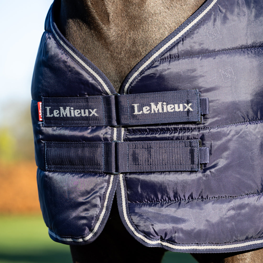 Detailbild des Brustverschlusses mit Klettverschluss an der LeMieux Unterdecke 100 g Navy pferdefreundlicher Komfort störungsfrei beim Liegen und Wälzen hält die Decke sicher in Position ideal als Liner-System mit nahtlos befestigter zweiter Linerdecke sorgt für optimale Stabilität und Flexibilität beim Layering von Pferdedecken. Das Lemieux Logo ist am Klettverschluss zu sehen.