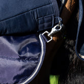 Detailaufnahme am Pferd der Schnellverschluss-Karabiner im Bereich der Hinterbeine am Deckenrock der LeMieux Unterdecke 100 g Navy. Die Karabiner sichern die Position der Unterdecke und ermöglichen die Befestigung einer zweiten Liner- oder Hauptdecke, um ein Verrutschen zu verhindern. Dieses System sorgt für flexibles, komfortables und pferdefreundliches Layering im LeMieux Pferdedecken Liner-System.