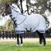 Ein Pferd mit erhobenem Kopf im Schatten trägt die graue Arika Armour-Tek Fliegendecke von LeMieux, die durch das antibakterielle Futter und den weichen Mähneneinsatz am Halsteil optimalen Tragekomfort ohne Scheuern bietet.