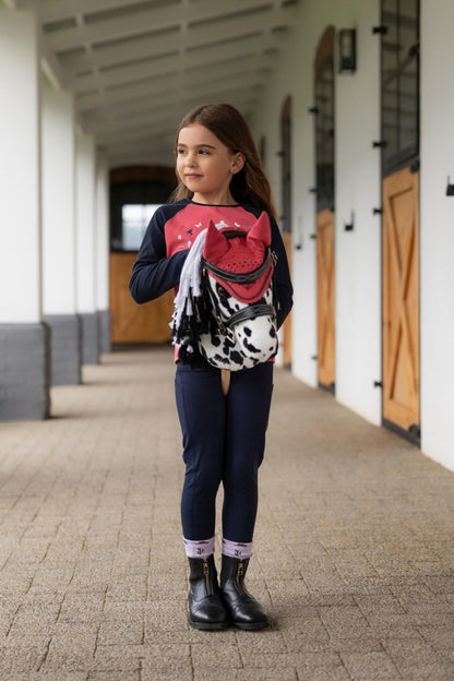 Kind steht mit dem LeMieux Hobby Horse Dakota Appaloosa Steckenpferd in der Stallgasse – realistisches Hobby Horse für Western, Dressur und Turniere von LeMieux. Das Hobby Horse trägt Hobby Horse Zubehör wie Trense und Fliegenohren.