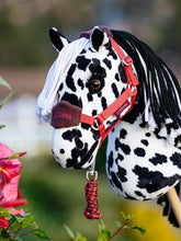 LeMieux Hobby Horse Halfter Vogue Cranberry mit Führstrick an Hobby Horse Dakota, einem weiß-schwarzen Tigerschecken, im Freien. Hochwertiges LeMieux Halfter für Hobby Horses mit verstellbarem Nasenriemen und Fleecepolsterung. Ideales Zubehör für realistische Hobby Horse Fotos, Outdoor-Training und kreative Reitspiele.