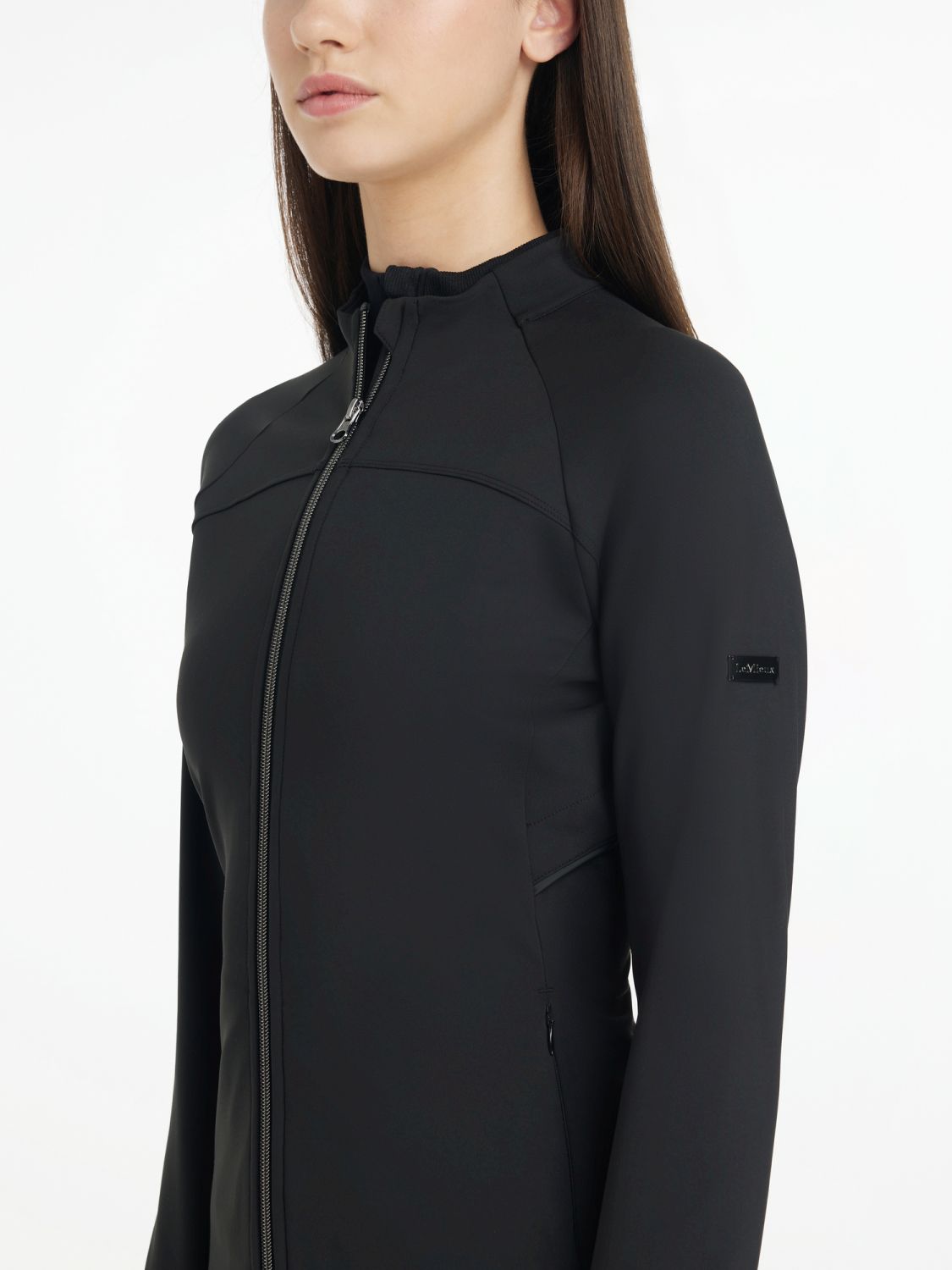 Das Model zeigt die sportliche LeMieux Jacke seitlich, so dass man das LeMieux Logo am Arm erkennen kann. Stilvoll, elegant und funktional für ambitionierte Reiterinnen, die Reitmode lieben. 