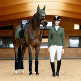Reiterin im LeMieux Turnieroutfit Jessica Mesh Pine Green steht in der Reithalle neben ihrem Pferd. Das perfekt abgestimmte Set umfasst die LeMieux Essence Schabracke und Fliegenmütze in Pine Green – ein eleganter Ton-in-Ton-Look für Pferd und Reiter.