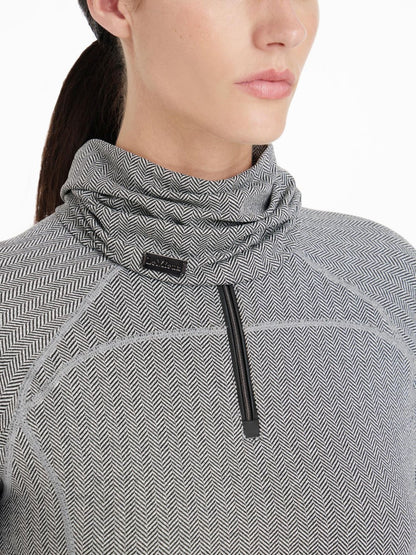 Der LeMieux Snood Aspen Herringbone mit Fischgrätmuster wird von dem Model kombiniert mit dem Aspen Herringbone Base Layer von Lemieux getragen. Der leichte Schlauchschal liegt locker um den Hals.Das Fischgrätmuster erinnert an die Gräten eines Fisches.