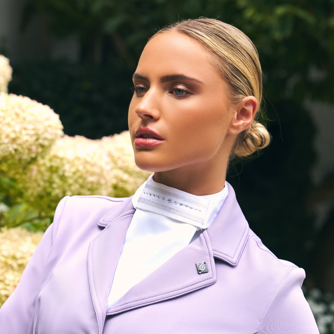 Reiterin trägt das Imperial Riding Plastron IRHBasic in Weiß zu einem hellen Turnierjacket in Wisteria, einem hellen Fliederfarbton. Vielseitig kombinierbares Turnierplastron für Dressur, elegante und dezente Kristallsteine mit silbernem Netzmuster, harmonisch abgestimmt für stilvolle Turnieroutfits im Dressursport.