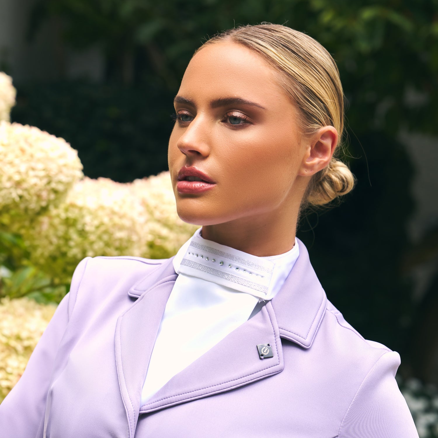 Reiterin trägt das Imperial Riding Plastron IRHBasic in Weiß zu einem hellen Turnierjacket in Wisteria, einem hellen Fliederfarbton. Vielseitig kombinierbares Turnierplastron für Dressur, elegante und dezente Kristallsteine mit silbernem Netzmuster, harmonisch abgestimmt für stilvolle Turnieroutfits im Dressursport.
