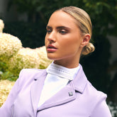 Reiterin trägt das Imperial Riding Plastron IRHBasic in Weiß zu einem hellen Turnierjacket in Wisteria, einem hellen Fliederfarbton. Vielseitig kombinierbares Turnierplastron für Dressur, elegante und dezente Kristallsteine mit silbernem Netzmuster, harmonisch abgestimmt für stilvolle Turnieroutfits im Dressursport.