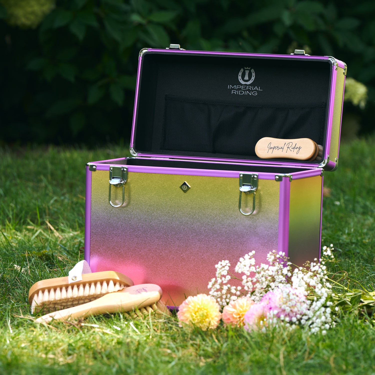 IRHBasic Slim Line Putzbox Unicorn von Imperial Riding draußen auf Gras, geöffneter Deckel mit Netztasche, flexible Innenaufteilung, Bürsten zur Pferdepflege sowohl in der Box als auch davor, Farbverlauf von Gelb zu Pink zu Lila, robust und stylisch für Stall und Turnier, funktionale Slim Line.