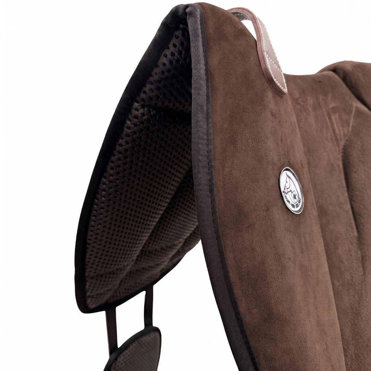 Die Detailaufnahme des braunen Brockamp Bareback Pad Reitpad Spezial zeigt das Reitkissen von vorne mit Blick auf die strukturierte, rutschfeste Anti-Slip-Unterseite aus Neopren im Übergang zur feinen Wildleder-Oberfläche. Erkennbar sind das runde Brockamp-Logo-Emblem, der braune Ledergriff mit Kontrastnaht und die robuste Kantenverarbeitung für optimalen Halt beim Reiten ohne Sattel.