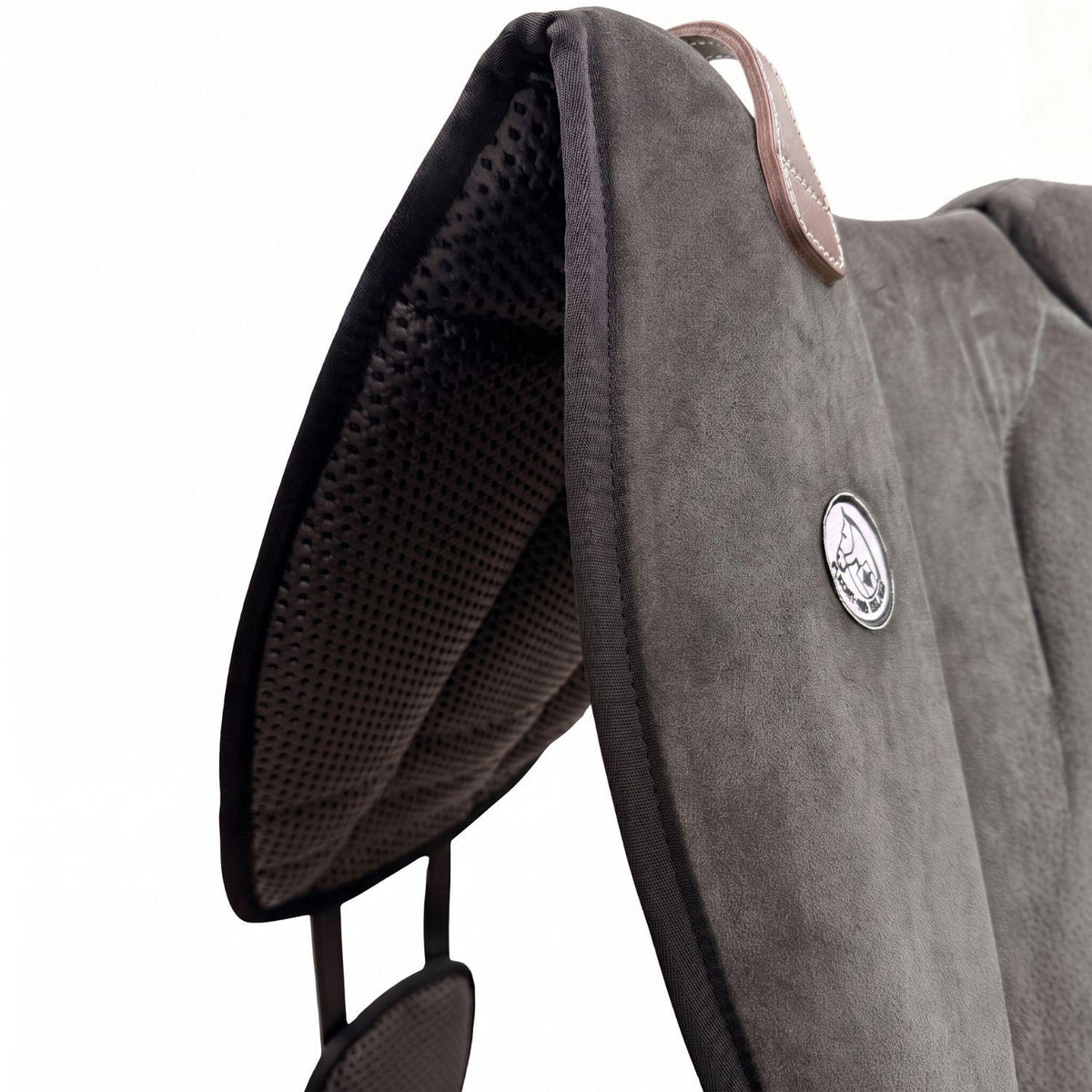 Die Detailaufnahme des dunkelgrauen Brockamp Bareback Pad Reitpad Spezial zeigt das Reitkissen von vorne mit Blick auf die strukturierte, rutschfeste Anti-Slip-Unterseite aus Neopren im Übergang zur feinen Wildleder-Oberfläche. Erkennbar sind das runde Brockamp-Logo-Emblem, der braune Ledergriff mit Kontrastnaht und die robuste Kantenverarbeitung für optimalen Halt beim Reiten ohne Sattel.