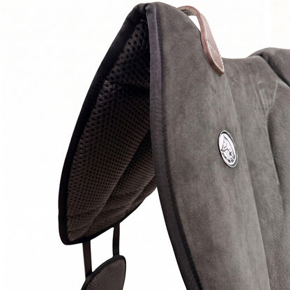 Die Detailaufnahme des dunkelgrauen Brockamp Bareback Pad Reitpad Spezial zeigt das Reitkissen von vorne mit Blick auf die strukturierte, rutschfeste Anti-Slip-Unterseite aus Neopren im Übergang zur feinen Wildleder-Oberfläche. Erkennbar sind das runde Brockamp-Logo-Emblem, der braune Ledergriff mit Kontrastnaht und die robuste Kantenverarbeitung für optimalen Halt beim Reiten ohne Sattel.