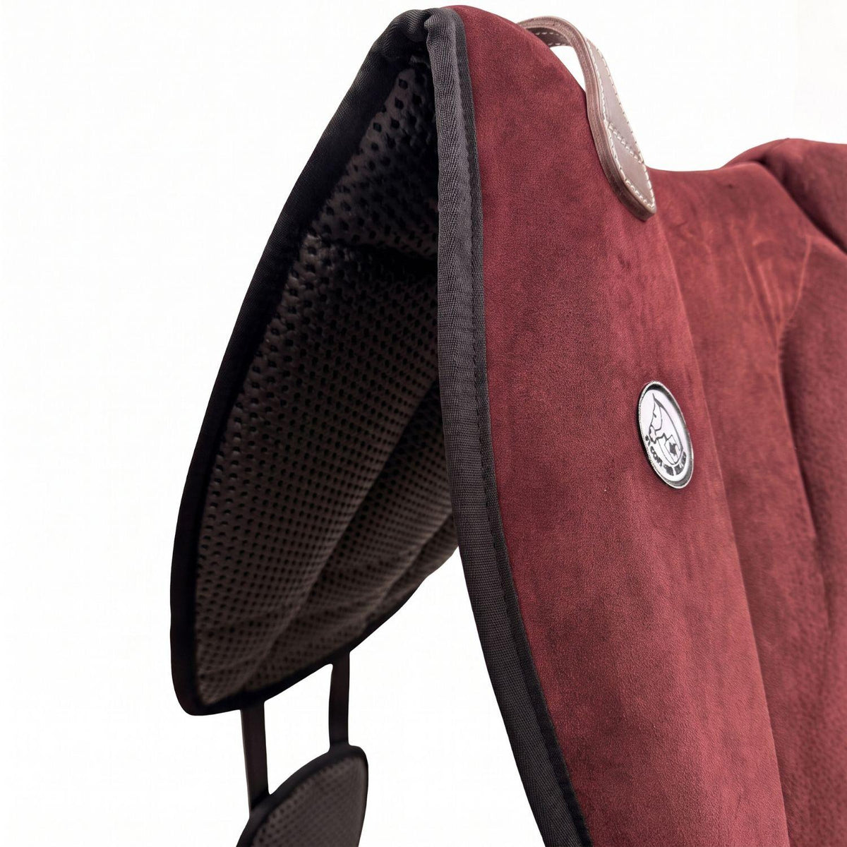 Die Detailaufnahme des dunkelroten Brockamp Bareback Pad Reitpad Spezial zeigt das Reitkissen von vorne mit Blick auf die strukturierte, rutschfeste Anti-Slip-Unterseite aus Neopren im Übergang zur feinen Wildleder-Oberfläche. Erkennbar sind das runde Brockamp-Logo-Emblem, der braune Ledergriff mit Kontrastnaht und die robuste Kantenverarbeitung für optimalen Halt beim Reiten ohne Sattel.