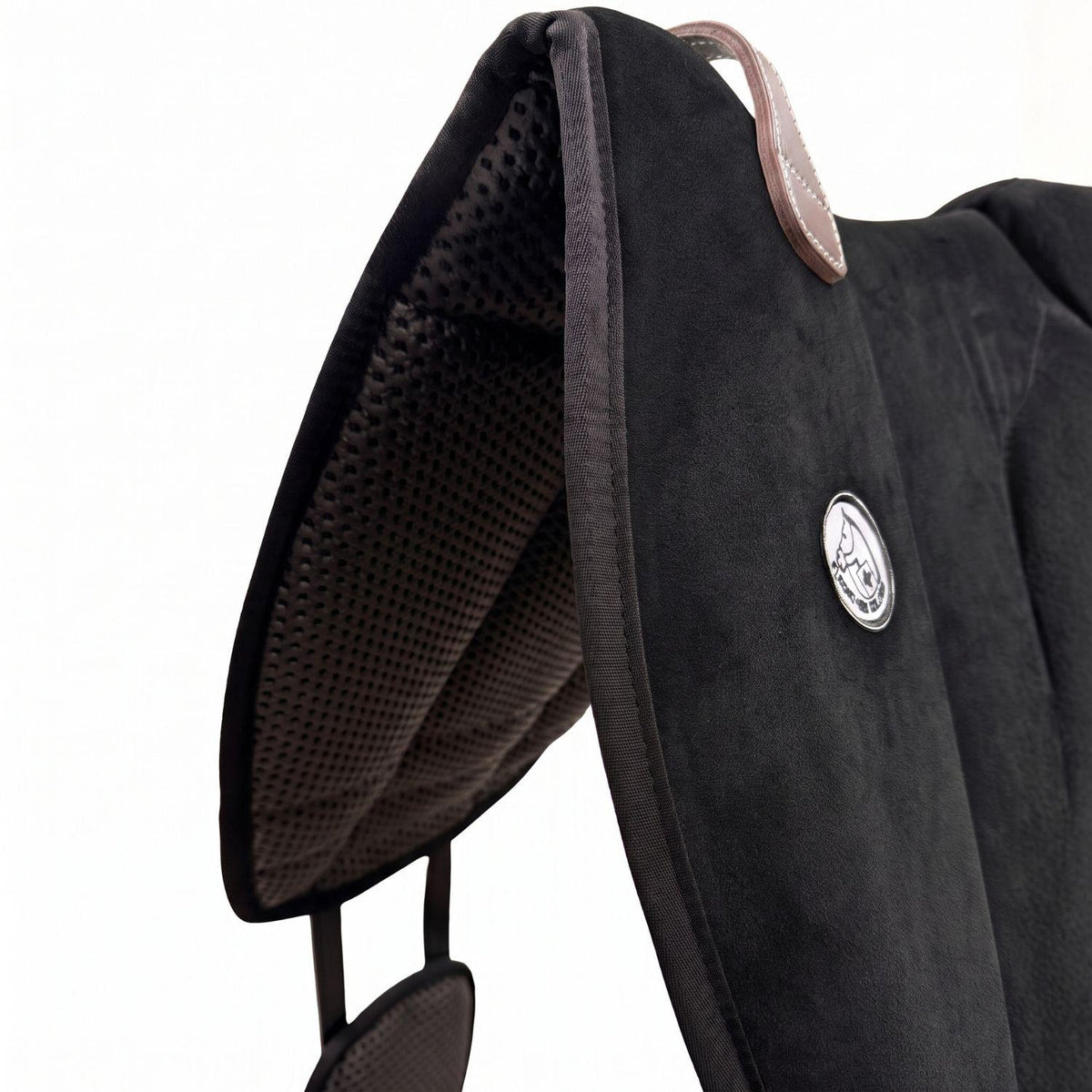 Die Detailaufnahme des schwarzen Brockamp Bareback Pad Reitpad Spezial zeigt das Reitkissen von vorne mit Blick auf die strukturierte, rutschfeste Anti-Slip-Unterseite aus Neopren im Übergang zur feinen Wildleder-Oberfläche. Erkennbar sind das runde Brockamp-Logo-Emblem, der braune Ledergriff mit Kontrastnaht und die robuste Kantenverarbeitung für optimalen Halt beim Reiten ohne Sattel.