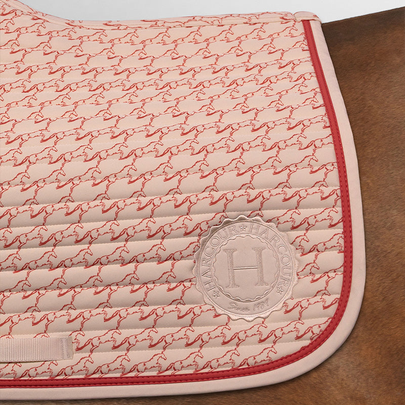 Großer hinterer Bildausschnitt der Harcour Schabracke Karembar Jump Shell Grapefruit. Zeigt den dynamischen Pferdeprint, die horizontale Steppung und die korallefarbene Litze. Beiges Harcour Logo. Absoluter Blickfang und sehr modische Sattelunterlage.