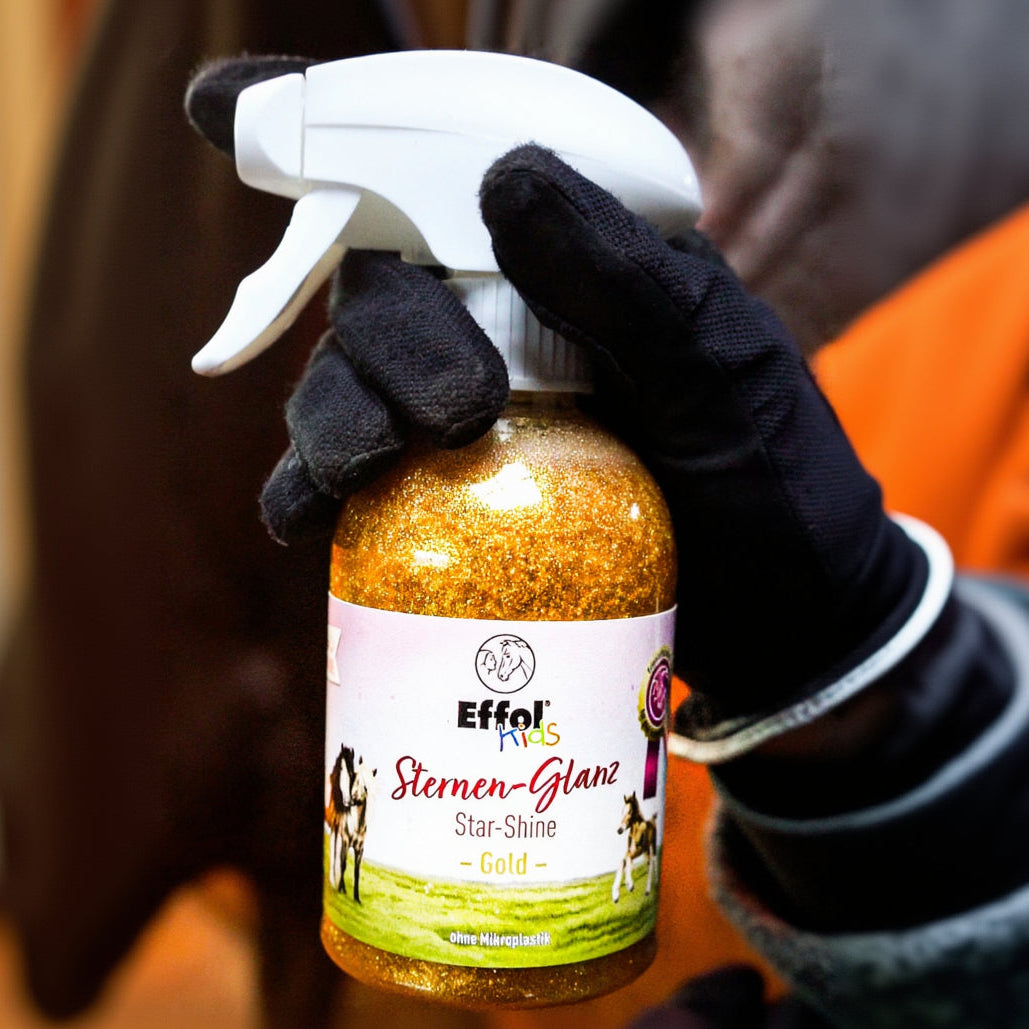 Reiterin hält die Effol Kids Sternen-Glanz Gold Sprühflasche in der Hand zum sprüen bereit. Im Hintergrund ist das Pony oder Pferd zu erkennen. Die Jubiläumsausgabe Effol Kids Sternen Glanz wird mit goldenen Glitzer als Glitterspray zelebriert. Effol ist schließlich der Goldstandard in der Pferdepflege für alle Pferdefreunde weltweit.