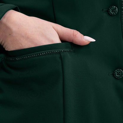 Detailaufnahme der rechten Einschubtasche des Harcour Damen Reitjackets Oria in Jungle. Eine Turnierreiterin schiebt ihre Handspitze in die praktische Tasche, welche edel mit funkelnder Glitzerlitze verziert ist. Durch diese sich wiederholenden Glitzer- und Designelemente entsteht ein harmonisches Gesamtbild der exklusiven Harcour Turnierbekleidung. Ein funktionales und zugleich stilvolles Turniersakko für Frauen, die auf dem Turnierplatz Wert auf durchdachte Details legen.
