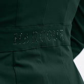 Seitliches Detailbild der Rückseite des Harcour Turnierjackets Oria in Jungle, einem Grünton. Im Bereich der Taille betont ein angedeuteter Bund den femininen Schnitt der Turnierjacke für Damen. Ein funkelnder Harcour-Logo-Schriftzug aus großen, grünen Strasssteinen ziert diesen Taillenbund. Dieses wunderschöne Glitzerdetail wertet die dezente Rückansicht auf und macht das Reitsakko für Markenfans zu einem echten Designerstück, das die weibliche Silhouette im Turniersport elegant in Szene setzt.